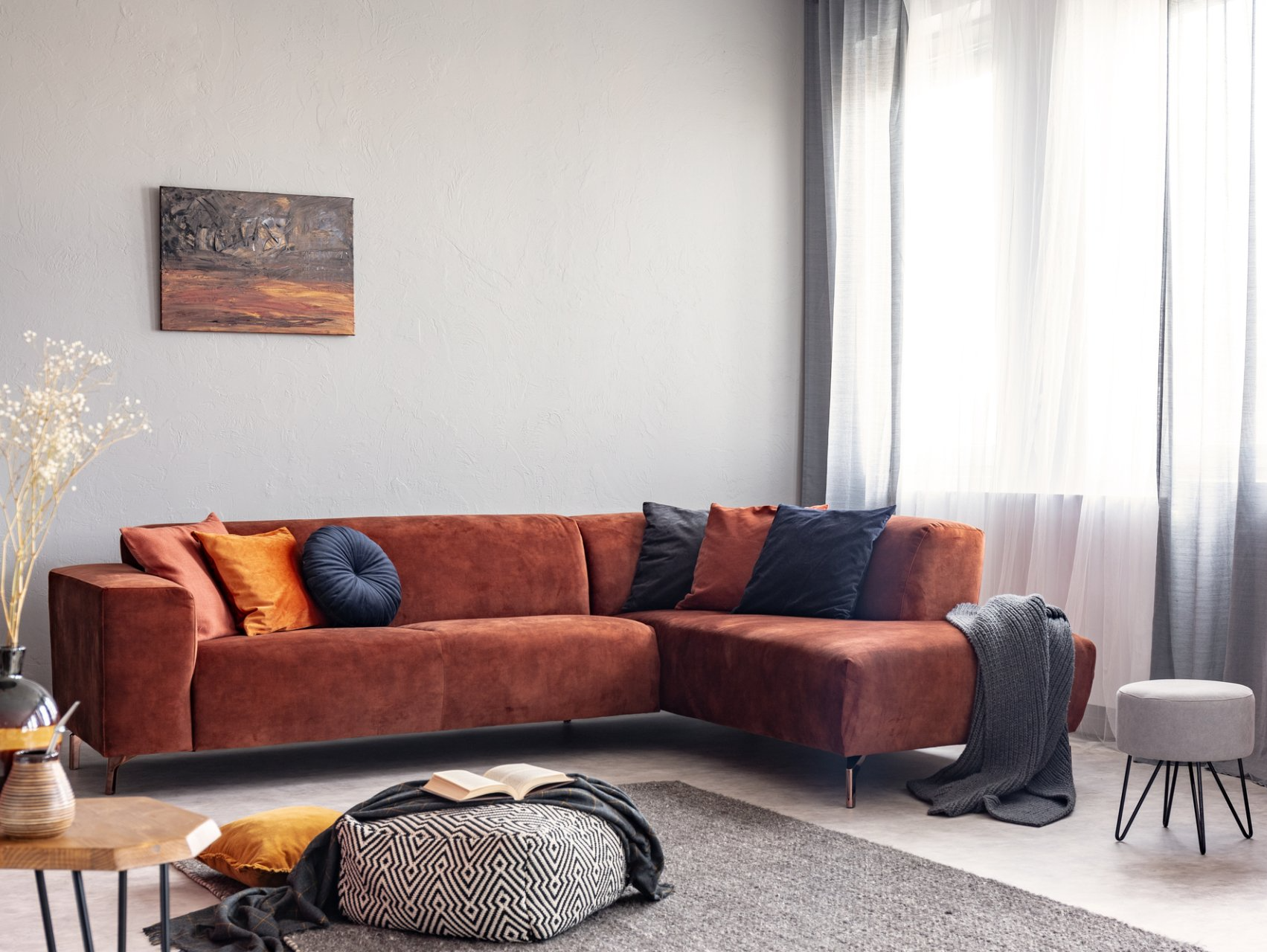 Rust coloured soft lounge with black and gold cushions in comfy lounge setting framed by grey curtains open over sheers letting light flow into the room.