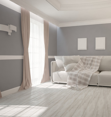 Neutral coloured room with curtains open over white sheers, letting sun shine in over neutral couch with cushions and throw rug.