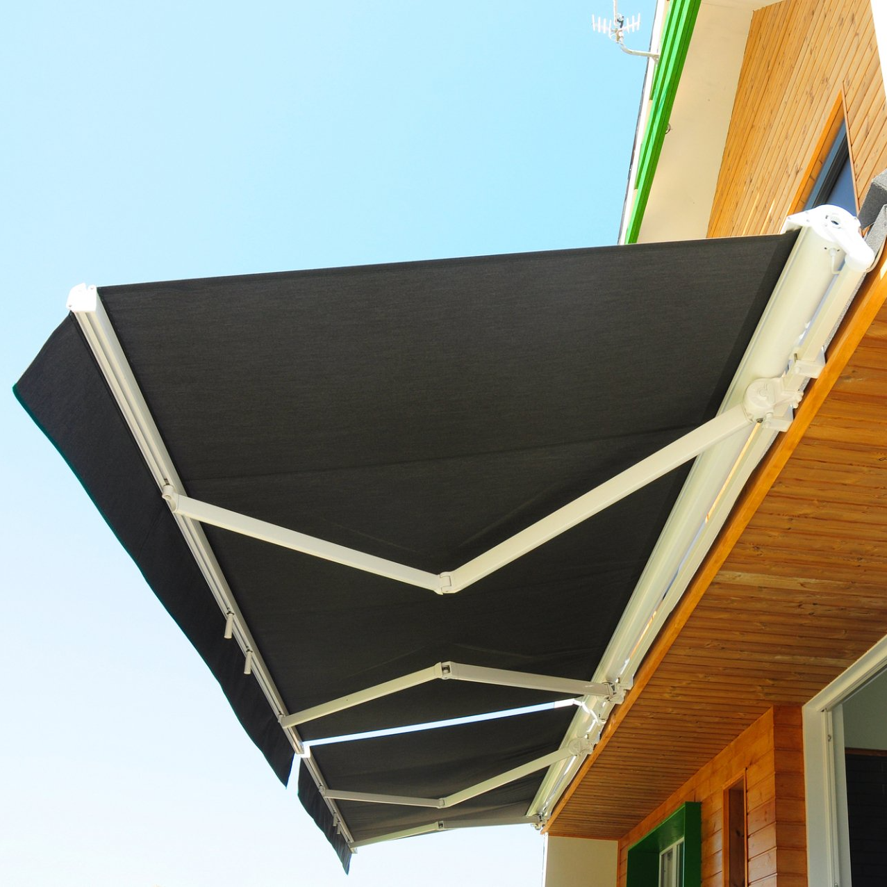 Black awning with white retractable arms, affixed to external wall of timber building.