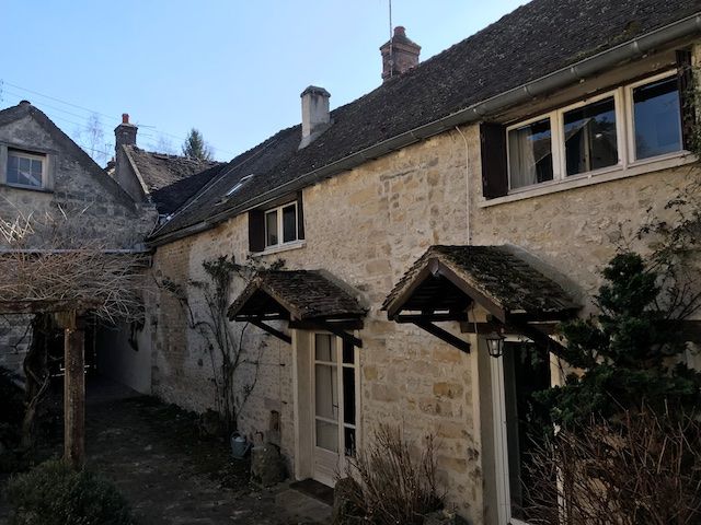 Stone cottages with dark wooden awnings and shutters. The setting is outdoors with a covered walkway on the left.