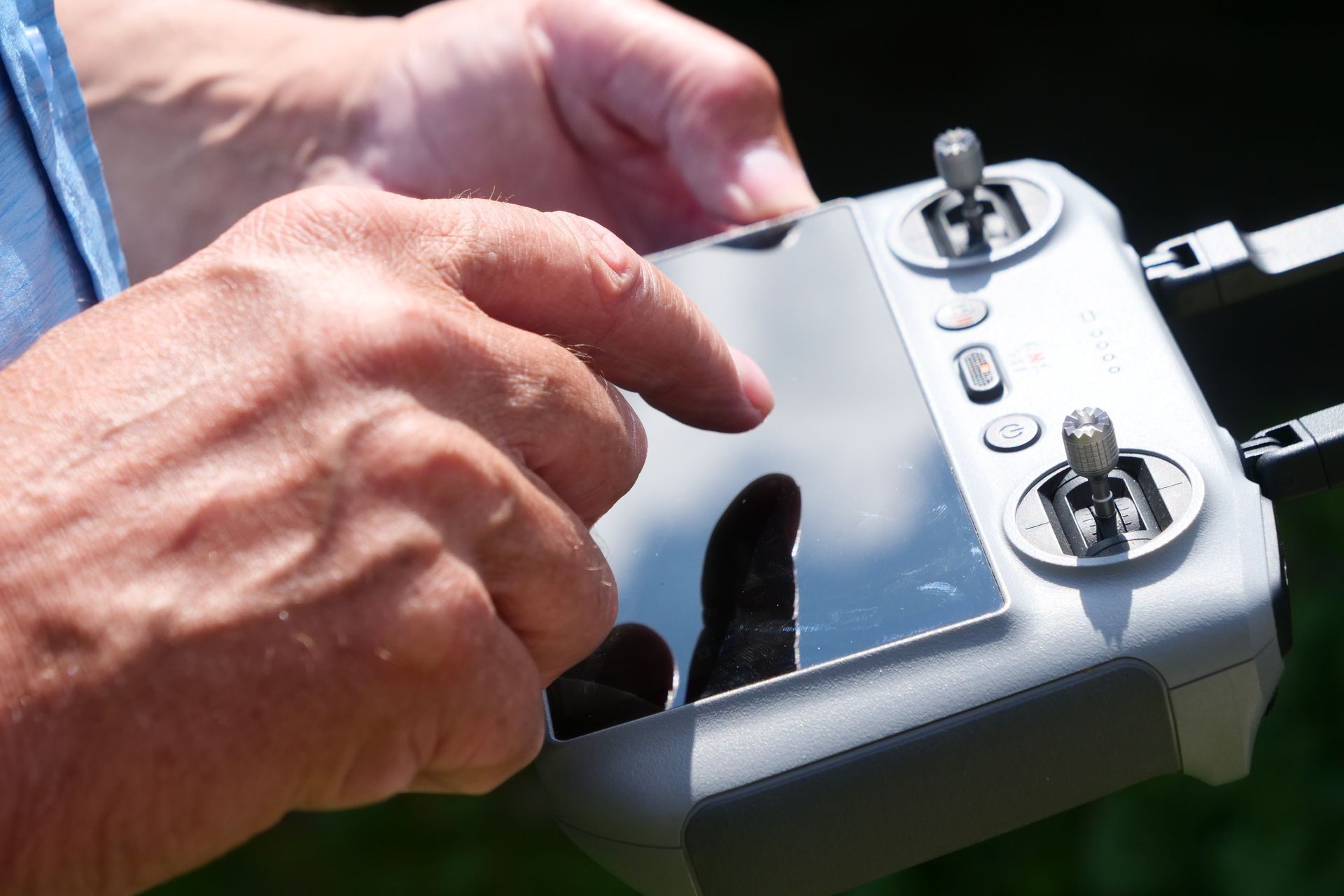 Close-up of a person's hands operating a drone controller with a touchscreen, outdoors.