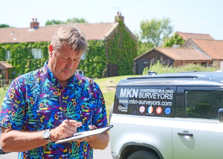 Man in colourful shirt outside, writing on a tablet near a white vehicle with 