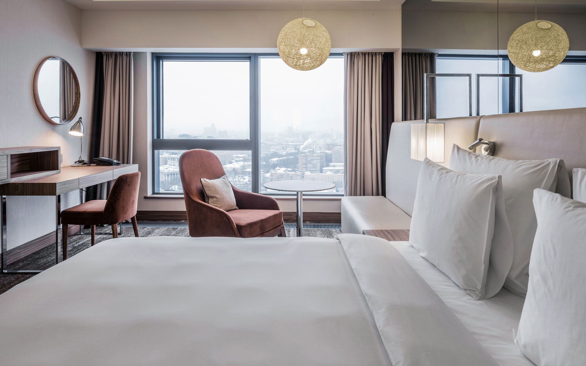 A hotel room with a bed , chair , desk and large window.