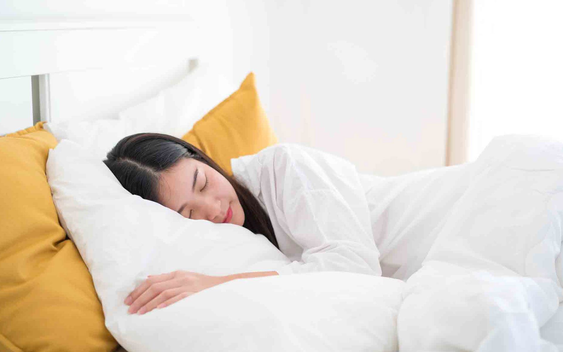 A woman is sleeping in a bed with white sheets and yellow pillows.