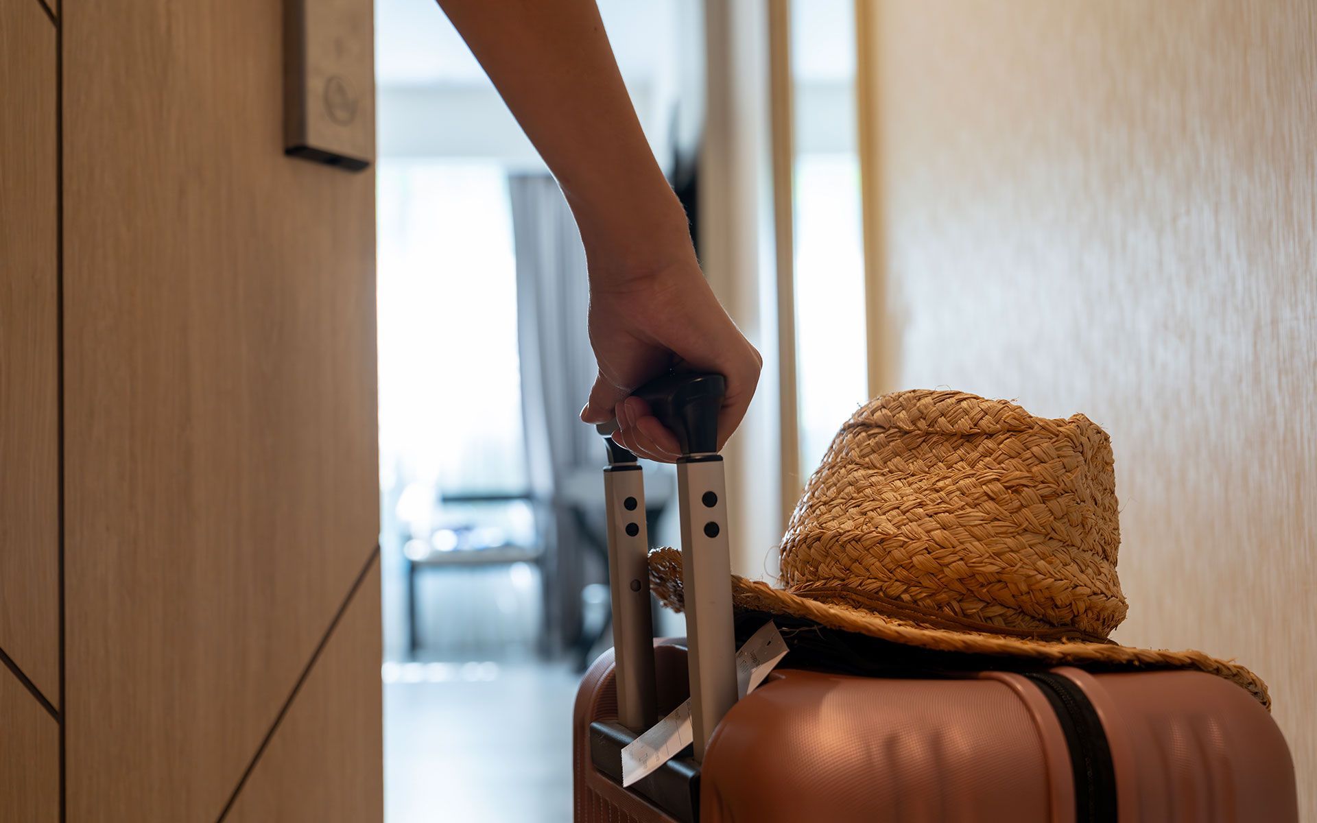 A person is pulling a suitcase with a hat on top of it.