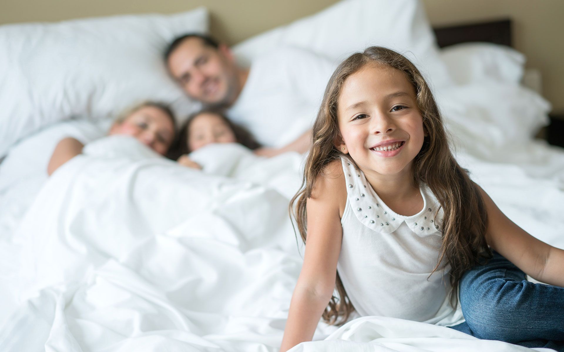 A little girl is sitting on a bed with her family.