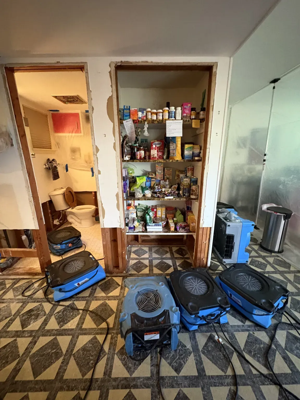 Small kitchen with patterned tile floor, open pantry shelves, and several blue backpacks on the floor.
