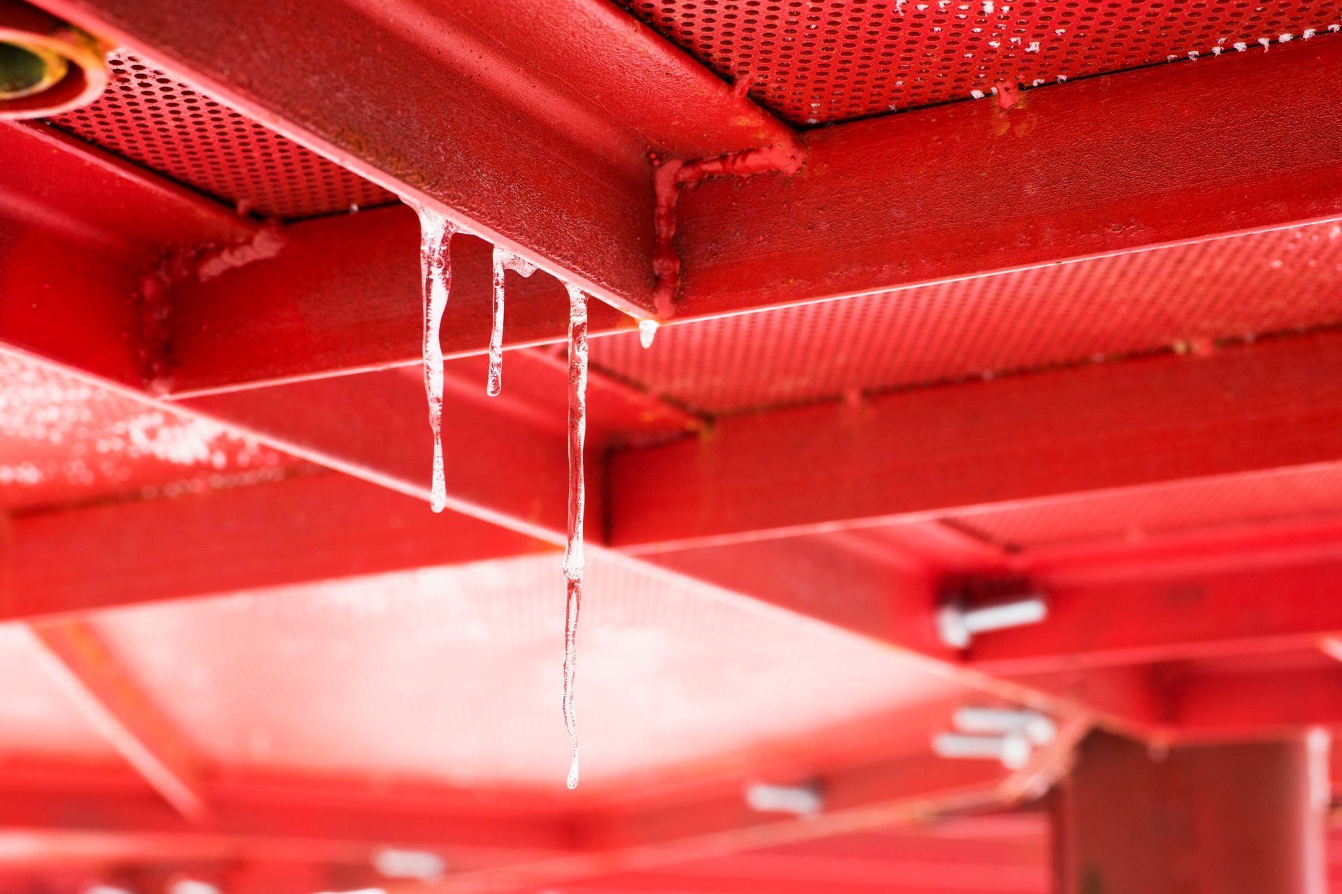 Red metal roof edge with icicles and dripping water in close-up