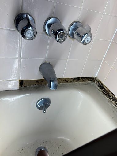 A bathtub with a faucet and three handles on the wall.