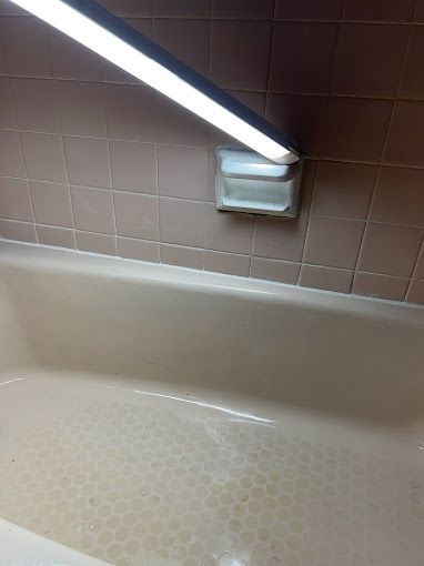 A bathtub in a bathroom with a light on the wall above it.