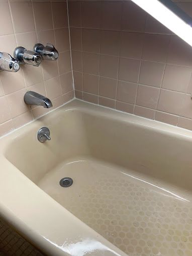 A bathtub in a bathroom with pink tiles and chrome faucets.