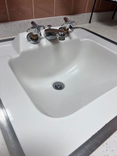 A bathroom sink with three faucets and a drain.