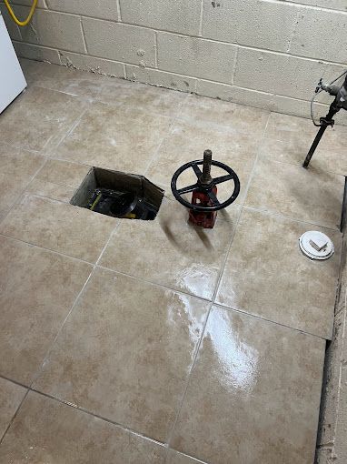 A valve is sitting on a tiled floor next to a hole in the floor.