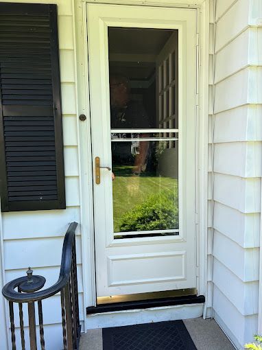 A white screen door is on the side of a white house.
