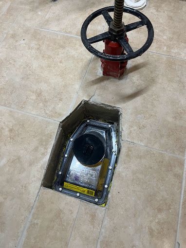 A red valve is sitting in a hole in the floor.