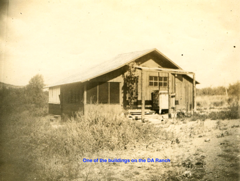 A weathered wooden building on a ranch with overgrown weeds. The building has a screened-in porch.