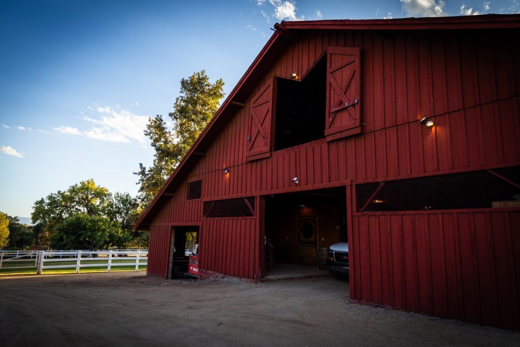Red barn with open doors, white fence, and blue sky.