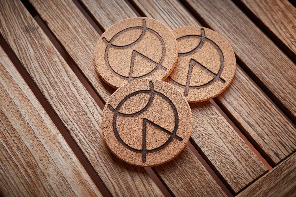 Three wooden coasters with a circular logo sit on a wooden table.