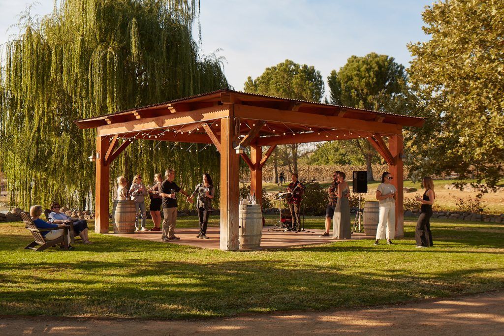 People dancing under a wooden pergola at an outdoor event, sunny day.
