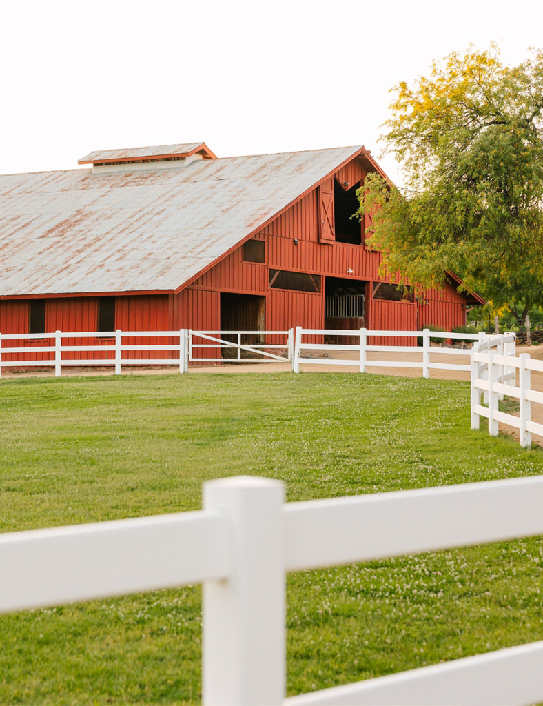 Red barn with white fence in a grassy field.