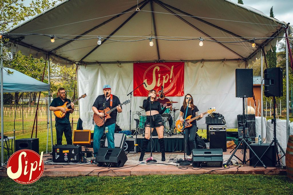 Band performing on stage under a white tent at an outdoor event.