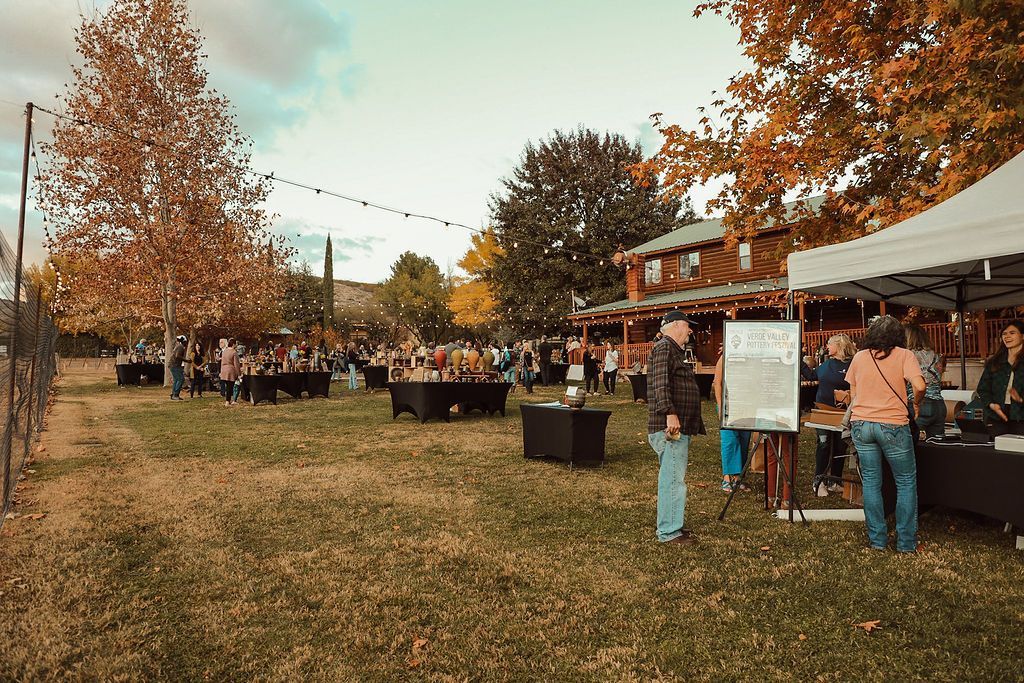 Outdoor event with people mingling; autumn colors, trees, tables, and a tent.
