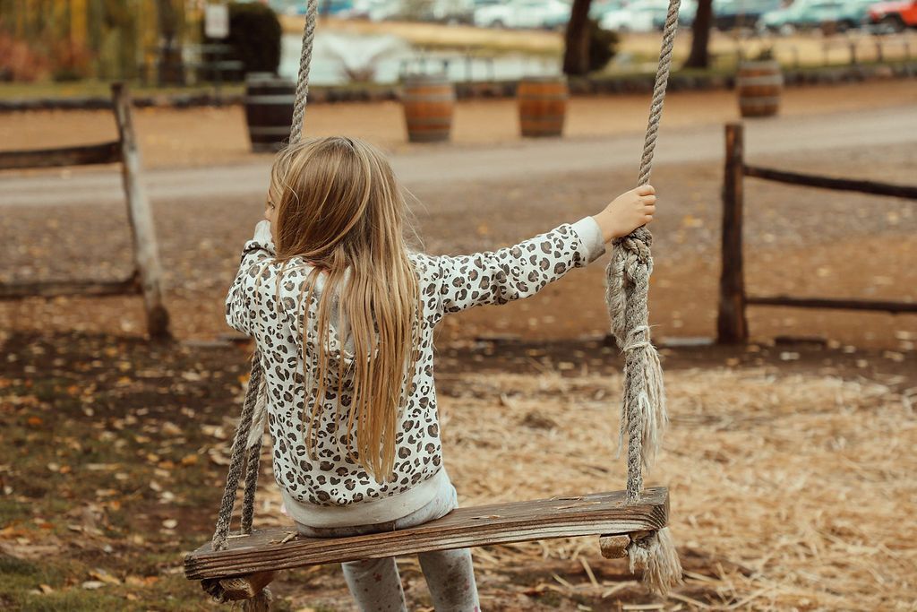 Girl on swing with long blonde hair, leopard print jacket, outdoors.