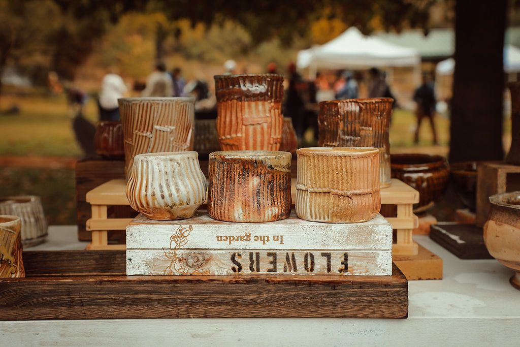 Ceramic pots for sale at a market, arranged on a wooden stand with a book that reads 
