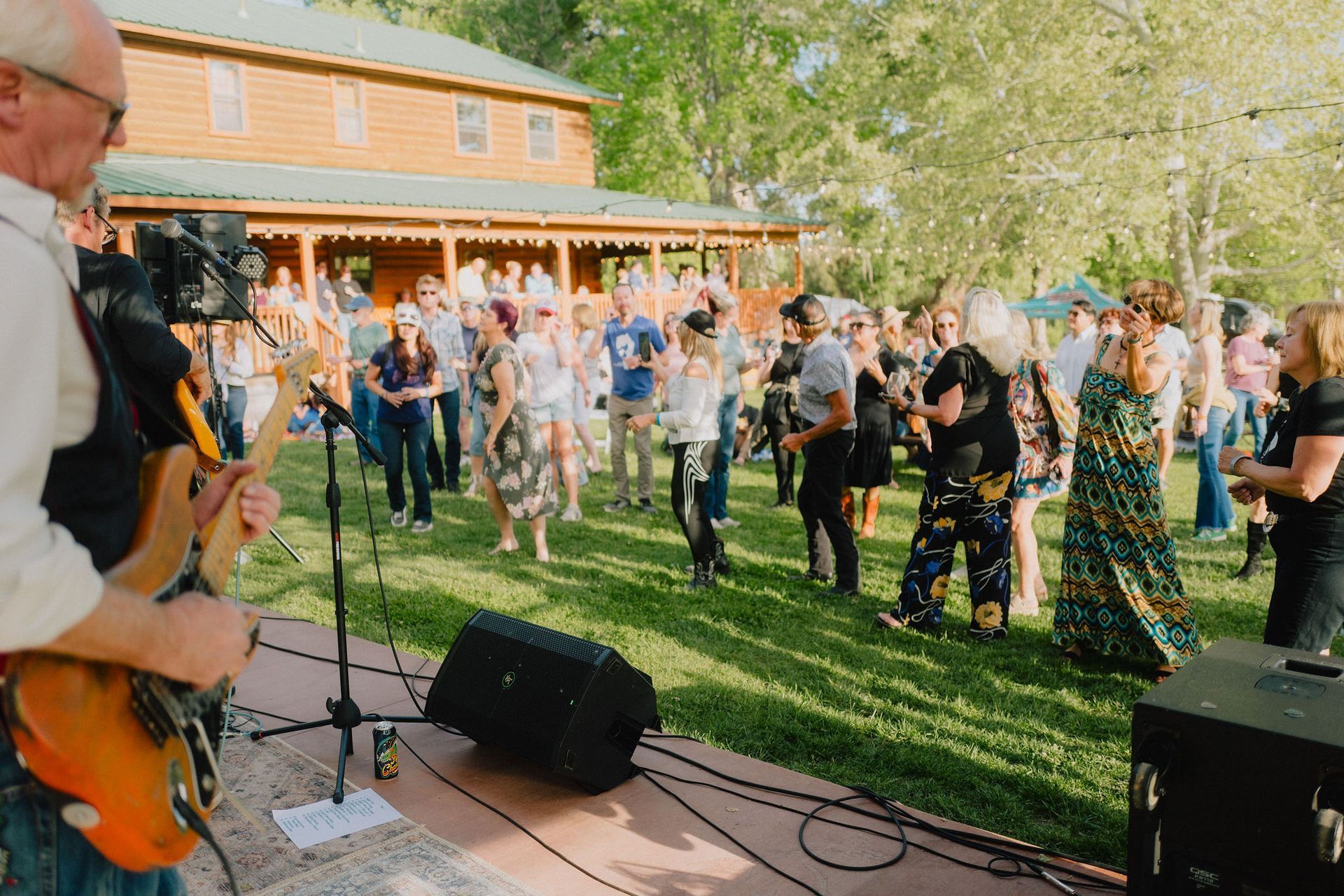 Band playing outdoors for a crowd dancing on grass near a wooden building.