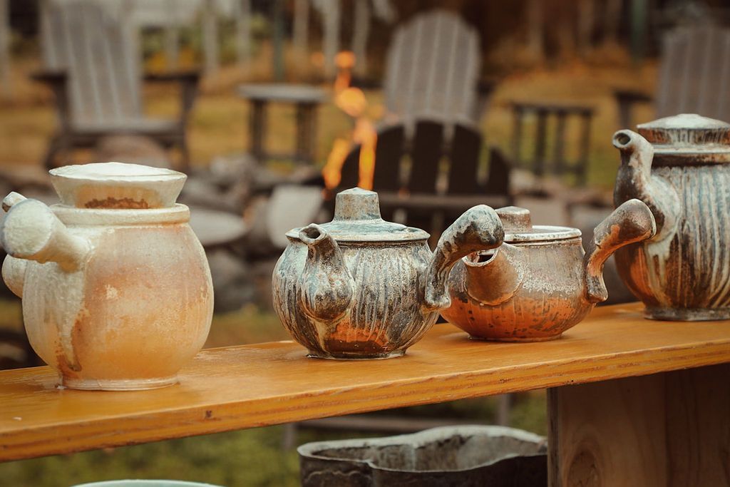 Ceramic teapots on a wooden shelf, outdoor setting with chairs and a fire pit visible in the background.