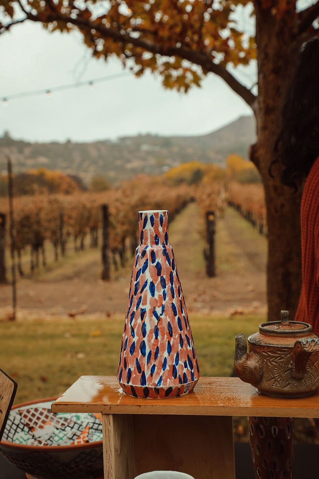 Ceramic vase with blue and pink design on a table in a vineyard.