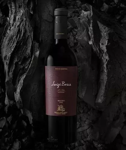 Una botella de vino tinto y dos copas de vino tinto en una mesa de madera.