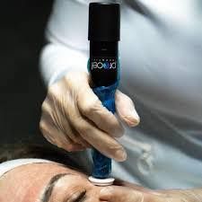 Cosmetic facial treatment on a woman lying down, with a gloved hand using a device on her cheek
