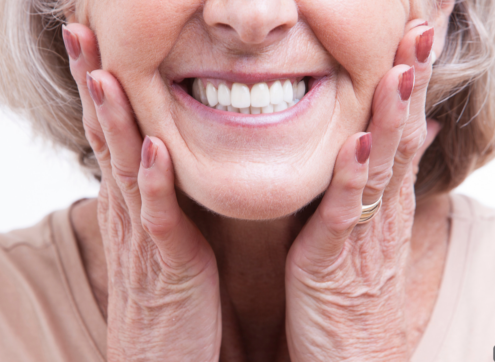 Smiling person touching their face with both hands, showing teeth and cheeks close-up