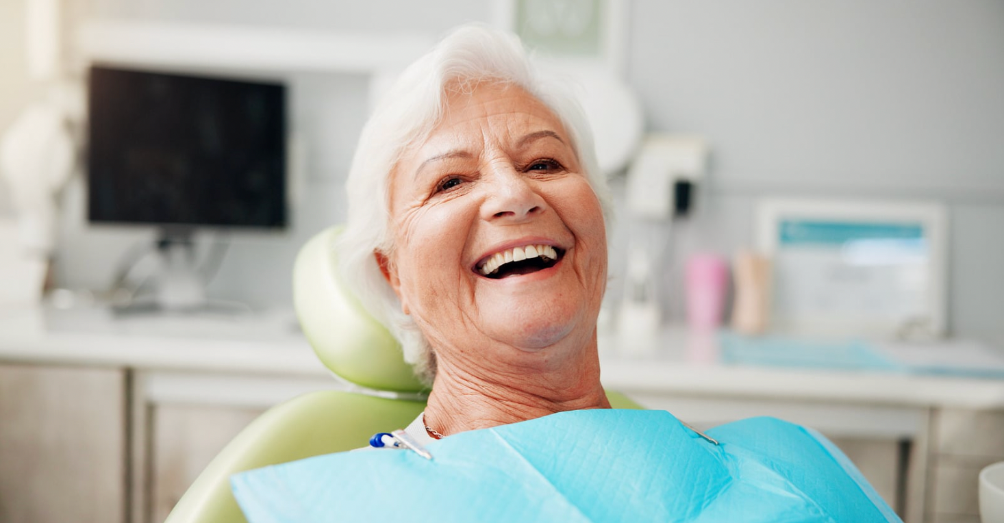Smiling person in a dental chair with blue bib in a bright clinic