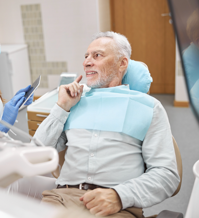 Patient in dental chair smiling while dentist works with blue gloves and bib in a clinic