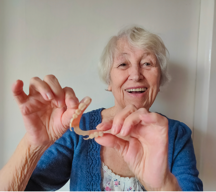 Smiling woman in a blue sweater holding a small necklace toward the camera