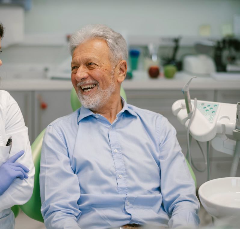 Smiling man in a light blue shirt sitting in a dental clinic chair, with dental tools nearby