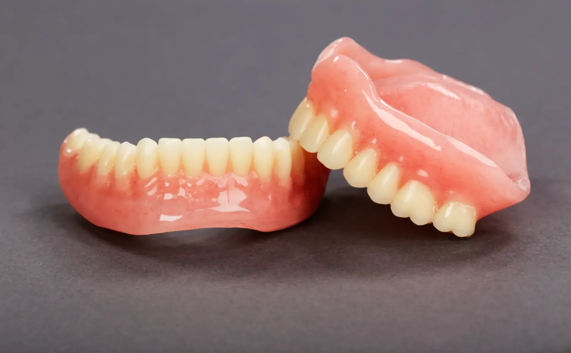 Two Pink Dentures With White Teeth on a Gray Background — Smiles On Hobart in Hobart, TAS