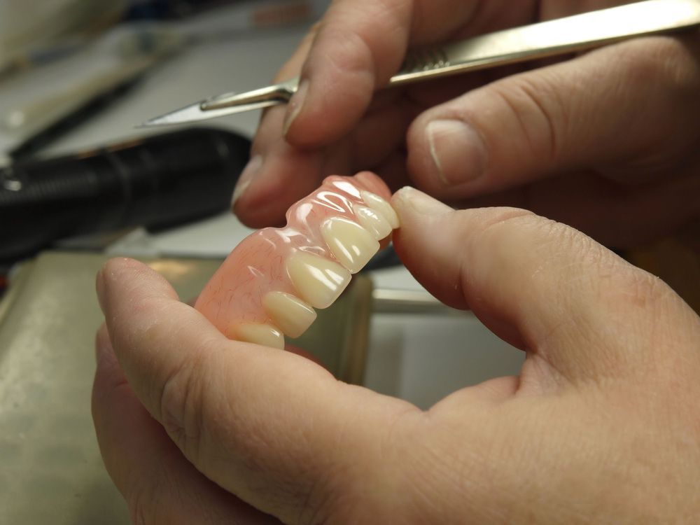 Hands Holding a Set of False Teeth With a Dental Tool Nearby — Smiles On Hobart in Sorell, TAS