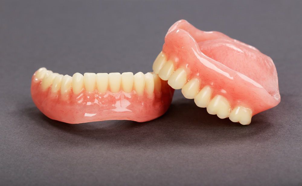 Two Pink Denture Sets With Cream Teeth on a Gray Background — Smiles On Hobart in Moonah, TAS