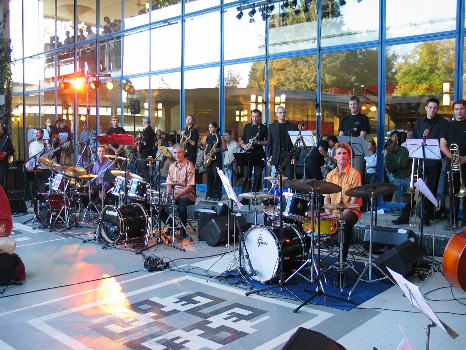 A big orchestra plays inside the CERN, with multiple drummers, classical, jazz and rock musicians.