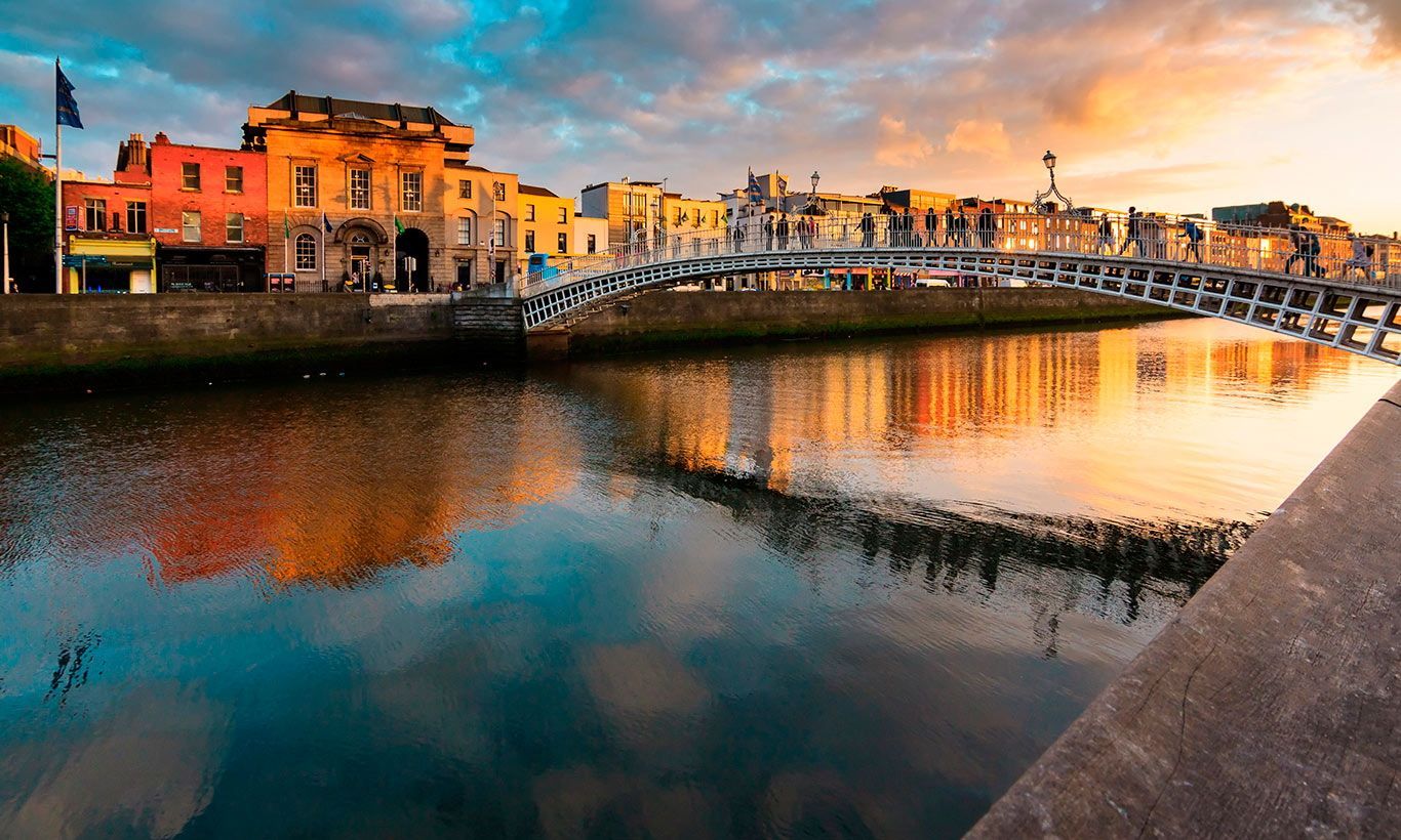 Ha’penny Bridge over the River Liffey in Dublin at sunset, reflecting the colorful sky in the water.