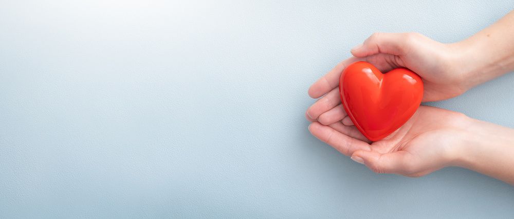 Hands holding a red heart on a light blue background