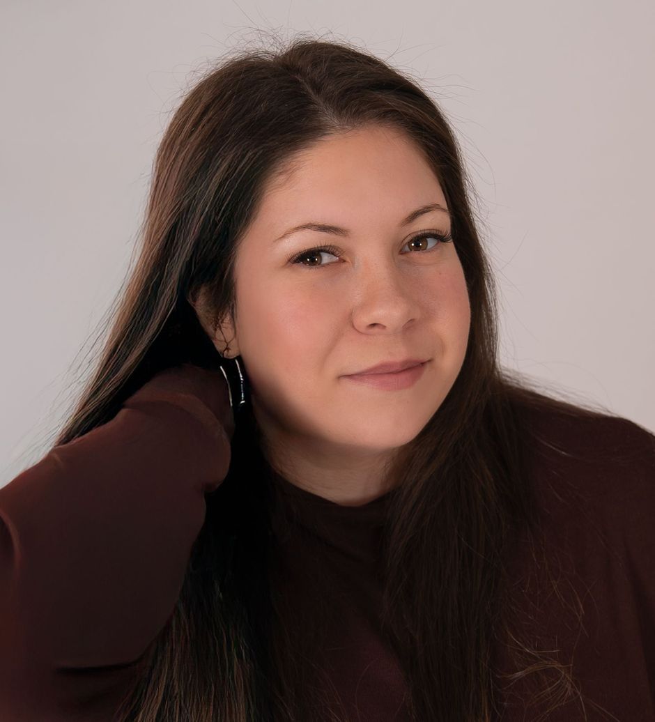 A woman with long hair is wearing a black sweater and smiling for the camera.