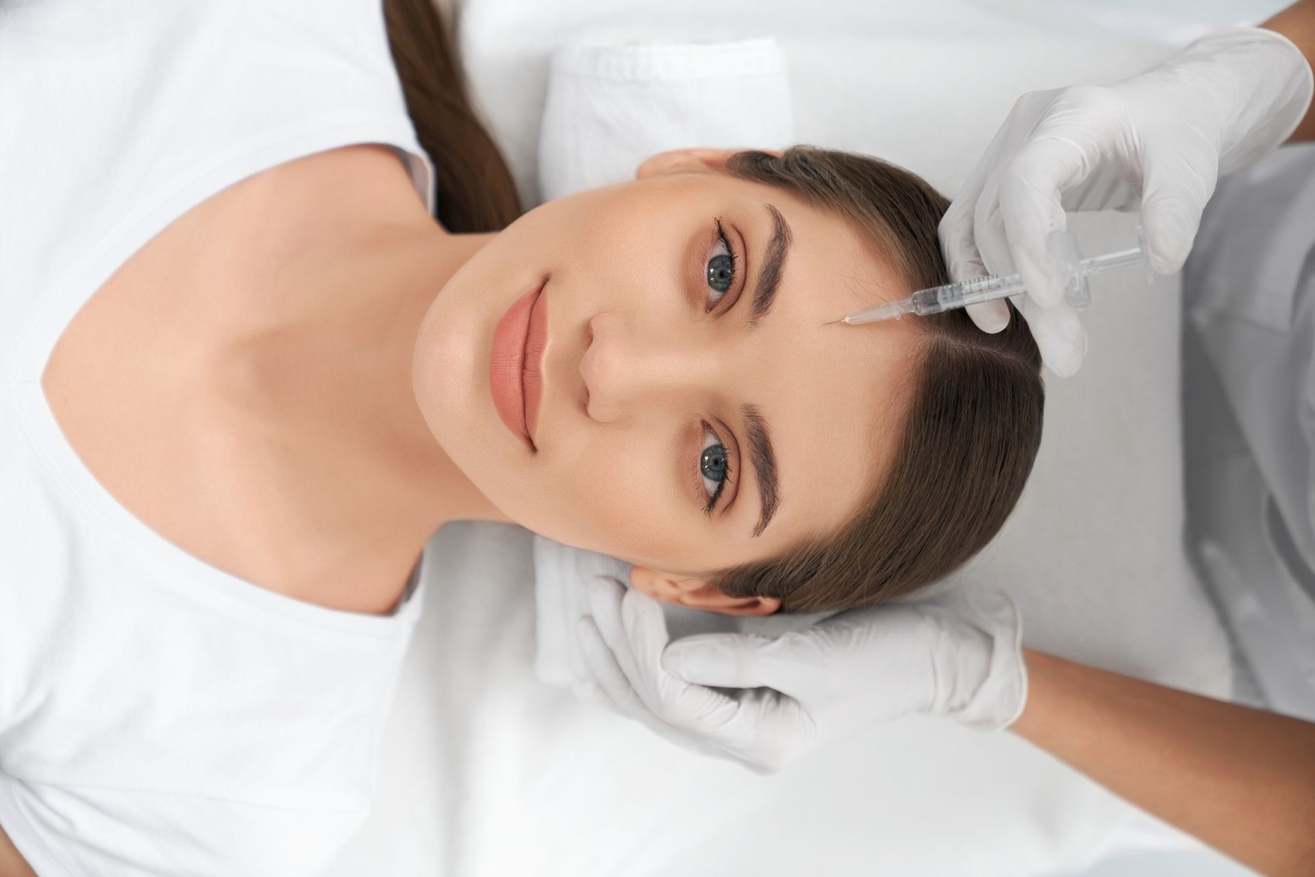 A woman is getting a botox injection in her forehead.