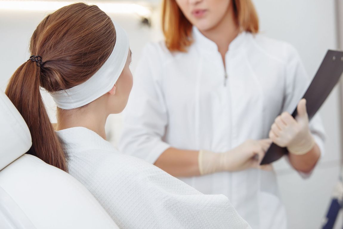 A woman is sitting in a chair talking to a doctor who is holding a clipboard.