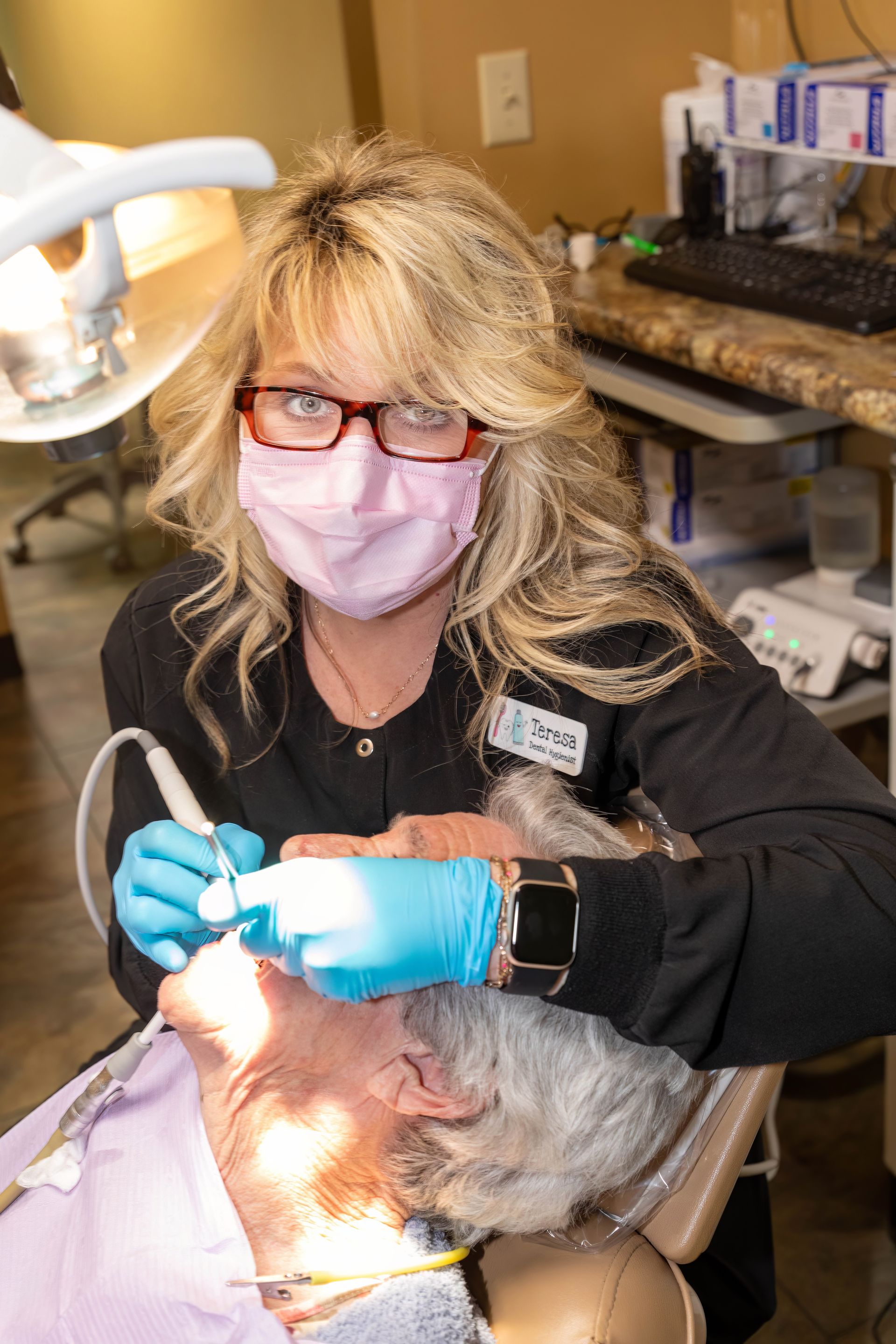 Dentist in mask and gloves examining a patient's teeth with dental tools in an office setting.