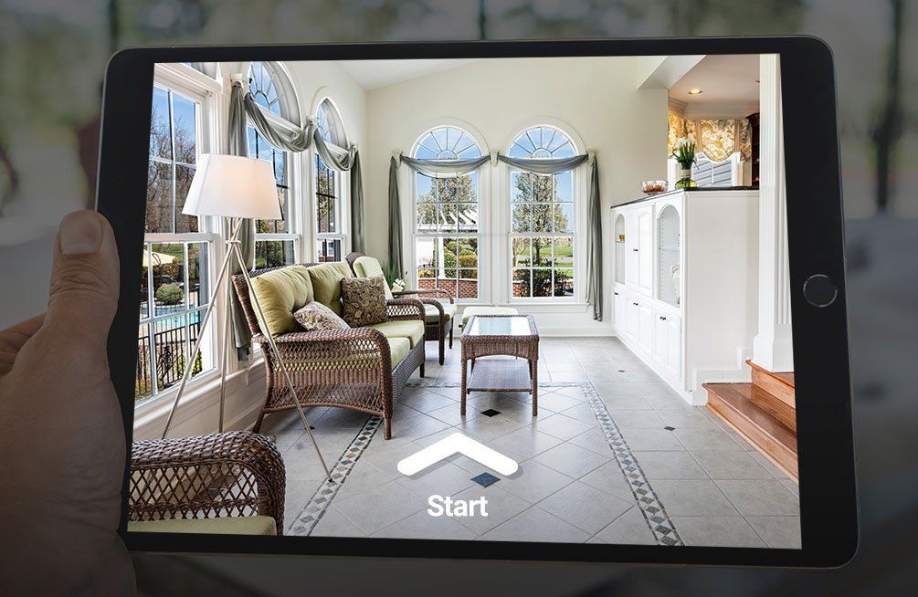 A person is holding a tablet with a picture of a living room on it.