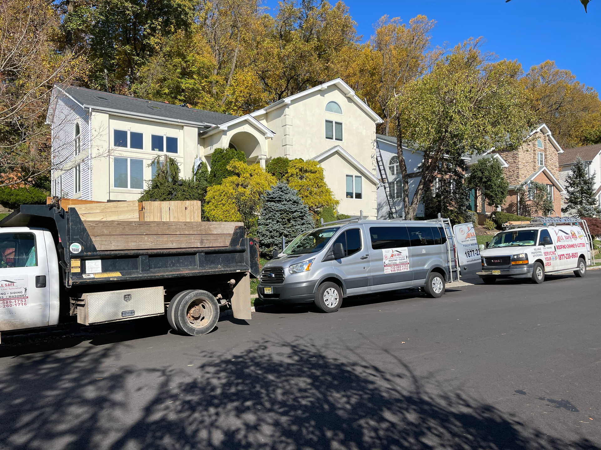All safe roofing dump truck and van are parked in front of construction site .